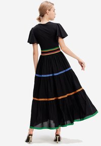 Robe maxi noire à manches courtes à volants, avec des accents en zigzag colorés en orange, bleu, vert et rouge à la taille et à l'ourlet.