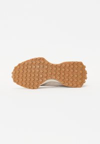 Semelle en caoutchouc d'une chaussure beige avec des crampons circulaires offrant de l'adhérence, vue par le dessous sur un fond blanc uni.