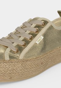 Χρυσό sneaker με υφή, μπεζ κορδόνια, χρυσά κορδόνια, πλεκτή πλατφόρμα και μια μικρή ετικέτα με την επιγραφή "ONLY" στην πλευρά.