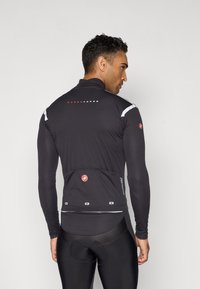 Veste de cyclisme noire ajustée avec des manches longues, trois poches arrière, des accents réfléchissants et un col haut pour plus de chaleur.