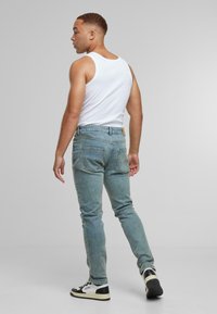 Vaaleansiniset slim-fit farkut, joissa on viisi taskua ja vaaleanruskea nahkafliitti takana vyötäröllä. Yhdistetty valkoiseen toppiin ja tennareihin.
