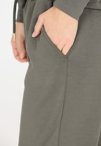 Olijfgroen zachte stof joggers met een zijzak. Heeft een relaxte pasvorm, zichtbare naaddetails en een verstelbare tailleband met drawstrings.