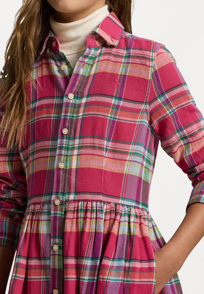 Karirana obleka v roza, zeleni in rumenih tonih. Ima gumbasto sprednjo stran, ovratnik, dolge rokave in zbrano krilo s stranskimi žepki.