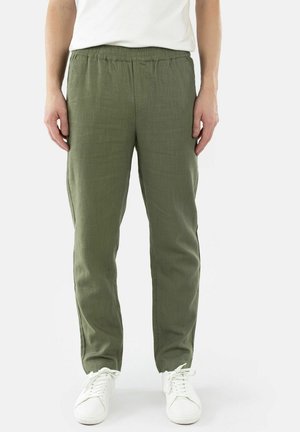 Mann iført olivengrønne bukser med elastisk midje og hvite joggesko, står mot en ensfarget hvit bakgrunn.