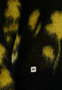 Pull en tricot avec une base noire et des taches jaunes, fabriqué en fil doux, avec une petite étiquette près du bas affichant un logo.