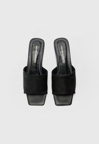 Fekete nyitott orrú slip-on mulyok széles szövetpánttal és elegáns négyzetes orral. Simács bőr talpbetéttel és kontrasztos varrással rendelkezik.