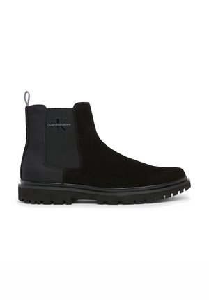 Botte Chelsea en daim noir avec panneau latéral élastique, languette de tirage marquée et semelle robuste pour une tenue décontractée masculine.