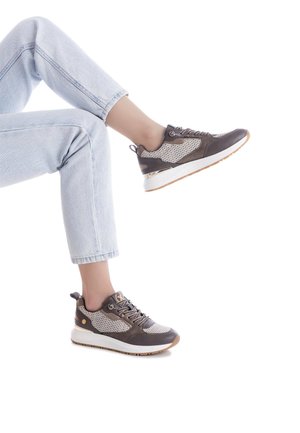 Zapatillas deportivas marrones y grises con paneles de malla, suela blanca gruesa y acentos de metal. Llevadas con jeans de color azul claro, mostrando un look casual.