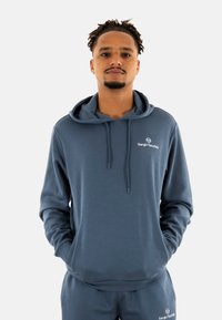 Sudadera con capucha en azul oscuro, con una textura suave y bolsillo tipo canguro en la parte frontal. Logo en el pecho, con cordones y dobladillo acanalado.