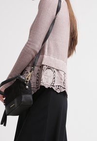 Maglione lavorato a maglia rosa pallido con orlo in pizzo, caratterizzato da motivi intricati. Abbinato a una borsa a tracolla in pelle nera.