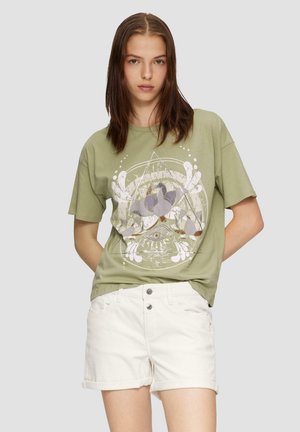 oliwkowa bawełniana koszulka z nadrukiem, luźny krój. W połączeniu z białymi szortami denimowymi z zapięciem na guziki i podwiniętymi nogawkami.