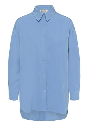 Helehall sinine pikkade varrukatega nööbitav särk terava krae ja veidi kõverdatud alläärega, millel on silt "Minu olulise garderoobi".