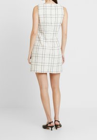 Vit ärmlös klänning med ett svart rutmönster, figurnära siluett och kort längd, även kombinerad med svarta klackskor.