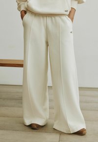 Kreemjas laia lõikega dressip üksid, millel on küljetaskud, peened õmblusdetailid ja pehme tekstuur. Sobivad kandmiseks pruuni värvi tossudega.