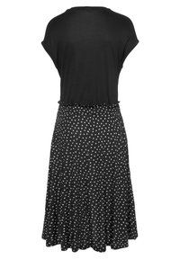 Schwarzes Kurzarmoberteil, das zu einem schwarzen Rock mit weißen Polka Dots übergeht. Der Stoff ist glatt, hat eine fließende Form und einen elastischen Bund.
