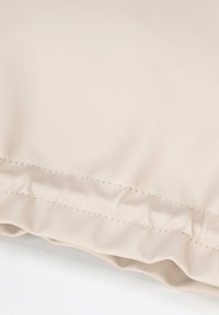 Cuscino sintetico beige con texture liscia, bordo arricciato e dettagli di cucitura a contrasto. Materiale resistente progettato per una facile pulizia.