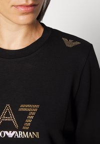 Zwarte sweatshirt met een ronde halslijn, versierd met gouden studs die "EA7" vormen en een logo op de schouder. Van een katoenmix.