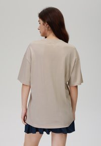 Beige oversized T-skjorte, korte ermer, glatt tekstur, rund hals, og en avslappet passform, parret med et mørkt denimskjørt.