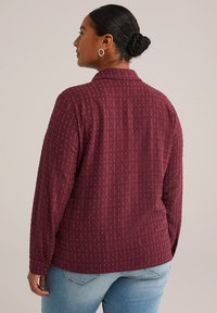 Camisa de manga larga burdeos con un patrón texturizado, cuello con cuello y puños abotonados; combinada con jeans de mezclilla azul claro.