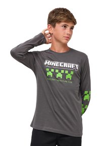 Szara koszula z długim rękawem z napisem "Minecraft Adventure Club" w białych i neonowo zielonych pikselowych akcentach na rękawach i na klatce piersiowej. Miękka tkanina.