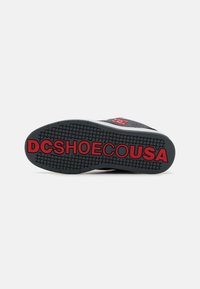 Talpa de pantof din cauciuc negru cu model texturat. Logo-ul "DCSHOECOUSA" scris cu litere roșii îndrăznețe, afișat proeminent. margini netede și toc circular.
