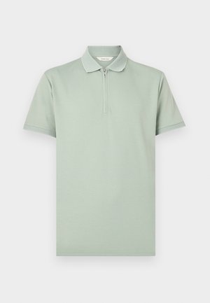 Lys grønn kortermet polo med glidelåsskjede på kragen og teksturert kant på krage og ermekanter, lagt flatt på hvit bakgrunn.