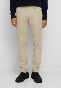 Beige chino's van katoen met een recht model, voorzien van zijzakken en een ritssluiting, gecombineerd met zwarte enkelboots.