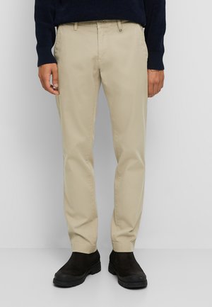 Beige chino's van katoen met een recht model, voorzien van zijzakken en een ritssluiting, gecombineerd met zwarte enkelboots.