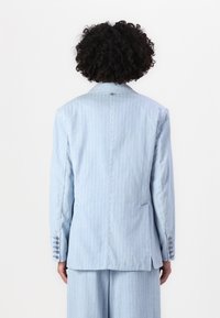 Blazer a righe blu chiaro con design sartoriale, rever a lancia e dettagli con bottoni sulle maniche. Tessuto liscio con una leggera lucentezza.