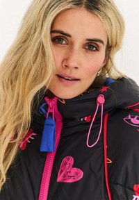 Černá prošívaná bunda s barevnými srdíčky a hvězdami, s růžovými a modrými doplňky, zipovým zapínáním a šňůrkami na kapuci.