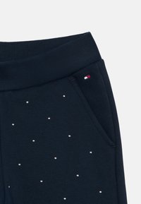 Navy sweatpants with a ribbed waistband, embellished with silver studs arranged in a dotted pattern, featuring a small logo patch.