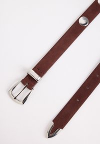 Ceinture en daim marron avec une boucle en métal argenté brillante, présentant une extrémité pointue et plusieurs trous pour un ajustement de taille.