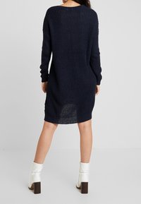 Marint ribbat stickad klänning med långa ärmar, midilängd och slits bak. Buren med vita ankelstövlar med en brun klack.