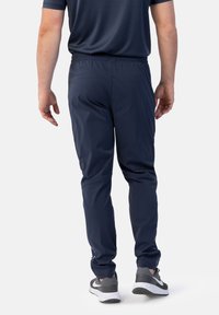 Marinefarbene Sporthosen mit elastischem Bund, schlank zulaufenden Beinen und seitlichen Reißverschlusstaschen, kombiniert mit grauen Sneakers mit weißer Sohle.