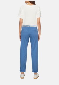 Niebieskie bawełniane spodnie o luźnym kroju, z mankietami na końcach nogawek i dwiema tylnymi kieszeniami. Noszone z białą koszulką z krótkim rękawem i białymi butami.