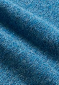 Nahaufnahme eines weichen, strukturierten blauen Wollstoffs mit sichtbaren Fasern und natürlichen Falten, die seine flauschige Oberfläche betonen.