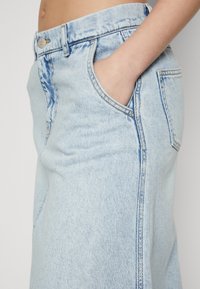 Lys blå denimskjørt med rett snitt, som har en sidelomme og synlige sømdetaljer. Stoffet ser mykt ut og er litt falmet.