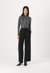 Sorte brede bukser med en tætsiddende metallic langærmet top, der har lodrette sølvstriber. Sorte hælede ankelstøvler fuldender outfittet.