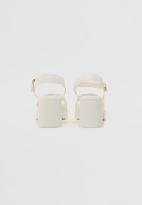 Sandales à talons blocs blanches avec brides de cheville, en cuir lisse. Présentent une boucle simple et un design ouvert, offrant stabilité et confort.
