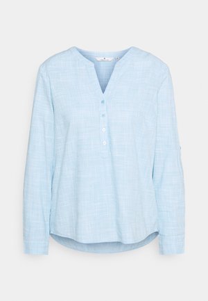 Lyseblå langærmet skjorte med V-hals, knaplukning og et struktureret ternet mønster. Materialet virker blødt og let gennemsigtigt.