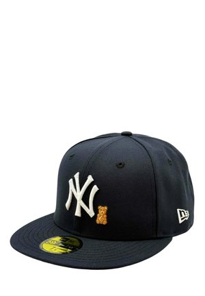 Tummansininen New York Yankees -lippis valkoisella logolla ja etuosassa pienellä ruskealla kirjotulla nallekarhulla, kullanvärinen kokotarra lippiksen lippaosassa.