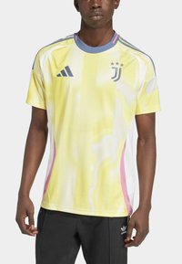 Gul meshtröja med en blå krage, rosa accentpaneler och en logotyp med tre stjärnor. Designad med korta ärmar och en avslappnad passform.