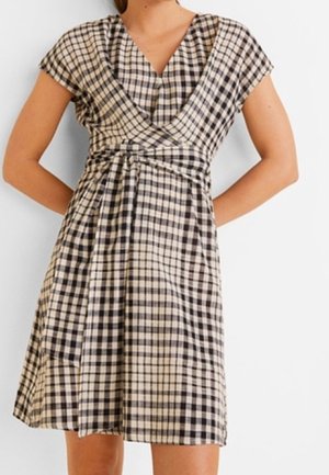 Nainen pukeutuneena polvipituiseen, lyhythihaiseen mustavalkoruudulliseen kietaisumekkoon, jossa on v-kaula-aukko ja vyötärönauha.