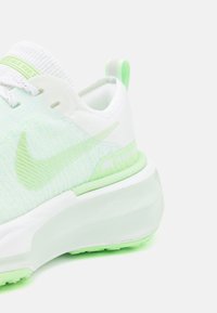 Chaussure de running Nike blanche et vert clair vue de profil avec logo Swoosh vert et semelle texturée sur fond blanc.