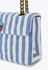 Sac à main matelassé avec des rayures bleues et blanches, bandoulière en chaîne et accent décoratif en forme de fraise rouge. Tissu texturé avec une forme structurée.