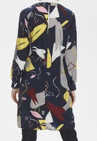 Tummansininen mekko, jossa on abstrakteja kuvioita keltaisessa, vaaleanpunaisessa ja harmaassa. Pitkät hihat, löysä malli ja takana nappikiinnitys. Silkkinen kangas.