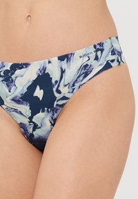 Blå og hvit mønstrete bikinitruse med lav skjæring, laget av glatt stoff. Har en logo nær midjebåndet.