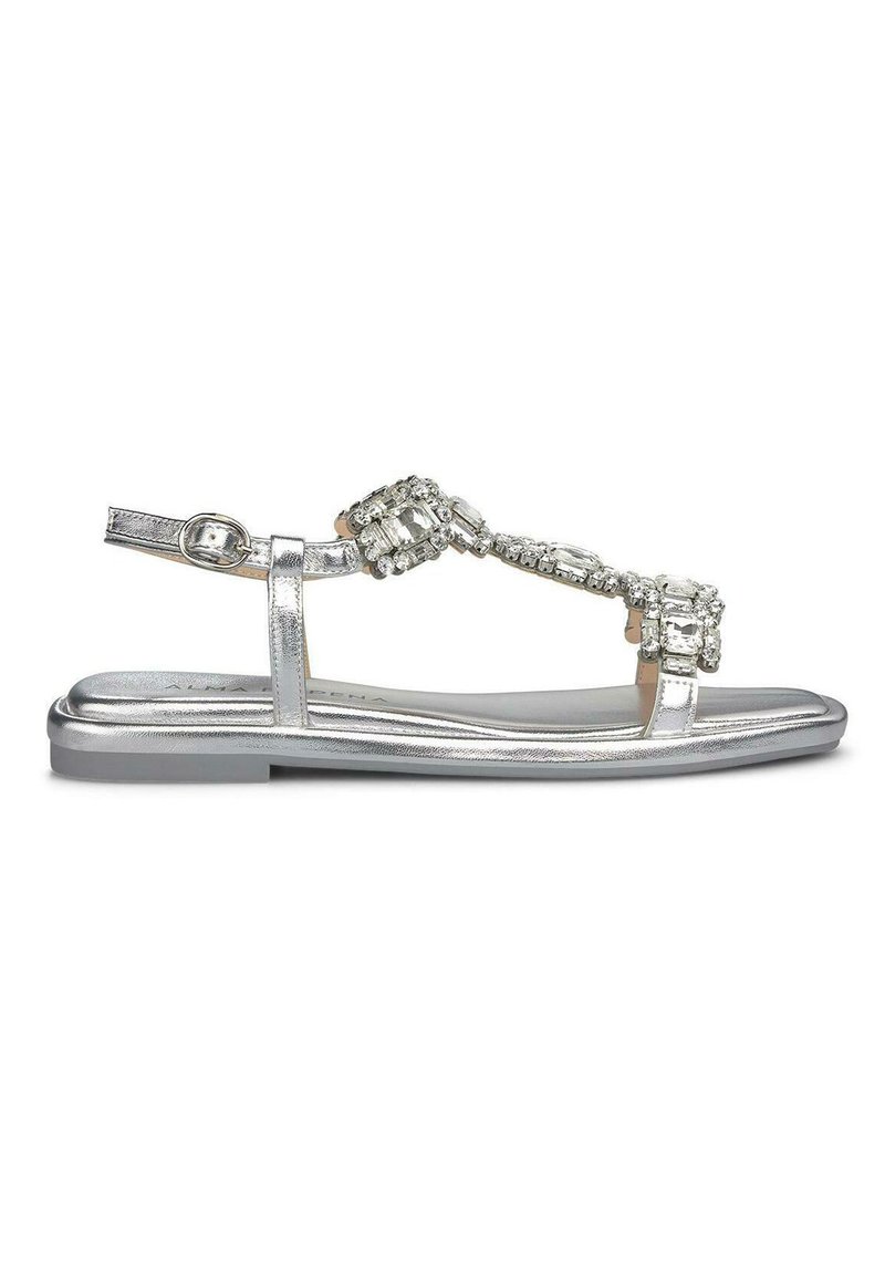 Sandalo piatto argento con design a T e decorazioni in strass, materiale sintetico e finitura metallica liscia.