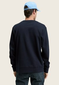 Sudadera azul marina hecha de tejido suave, con mangas largas y cuello redondo. La parte trasera es lisa, con dobladillo y puños acanalados.