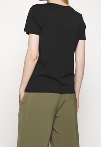 Černé bavlněné tričko s krátkým rukávem a kulatým výstřihem, zobrazené zezadu, spojené s olivově zelenými kalhotami, uvolněný střih.